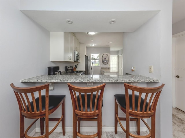 418 Cerromar Ct Unit 158, Venice, FL 34293 - kitchen with appliances with stainless steel finishes, white cabinets, a peninsula, and light stone countertops