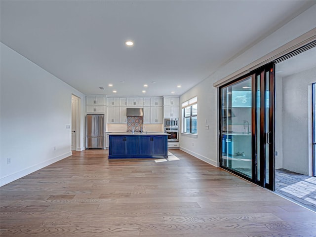 12705 Pinnacle Ln, Venice, FL 34293 - kitchen with appliances with stainless steel finishes, white cabinetry, range hood, light wood-type flooring, and a sink