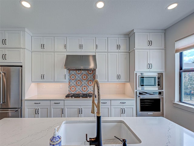 12705 Pinnacle Ln, Venice, FL 34293 - kitchen featuring appliances with stainless steel finishes, exhaust hood, a sink, white cabinetry, and tasteful backsplash