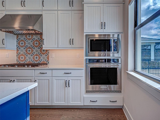12705 Pinnacle Ln, Venice, FL 34293 - kitchen featuring stainless steel appliances, wall chimney exhaust hood, backsplash, wood finished floors, and baseboards