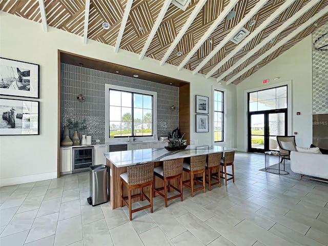 12705 Pinnacle Ln, Venice, FL 34293 - kitchen with wine cooler, a kitchen bar, light stone counters, high vaulted ceiling, and tasteful backsplash