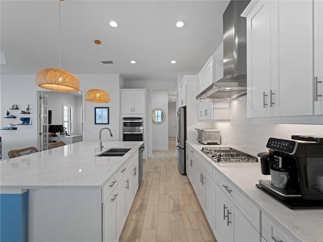 13056 Steinhatchee Loop, Venice, FL 34293 - kitchen featuring a sink, wall chimney range hood, appliances with stainless steel finishes, an island with sink, and white cabinets