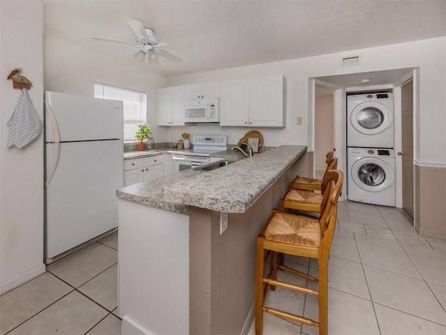 25050 Sandhill Blvd Unit 6A3, Punta Gorda, FL 33983 - kitchen with white appliances, stacked washer and clothes dryer, a peninsula, white cabinetry, and light tile patterned floors