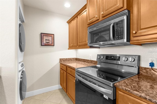 235 Base Ave E Unit 207, Venice, FL 34285 - kitchen featuring stainless steel appliances, stacked washing machine and dryer, light tile patterned flooring, and brown cabinetry