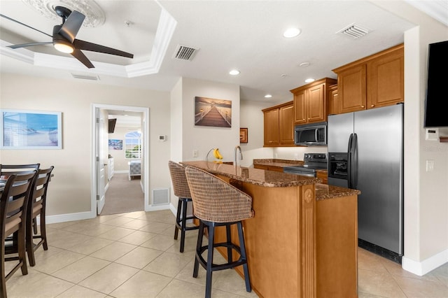 235 Base Ave E Unit 207, Venice, FL 34285 - kitchen with appliances with stainless steel finishes, brown cabinetry, dark stone countertops, a ceiling fan, and a breakfast bar