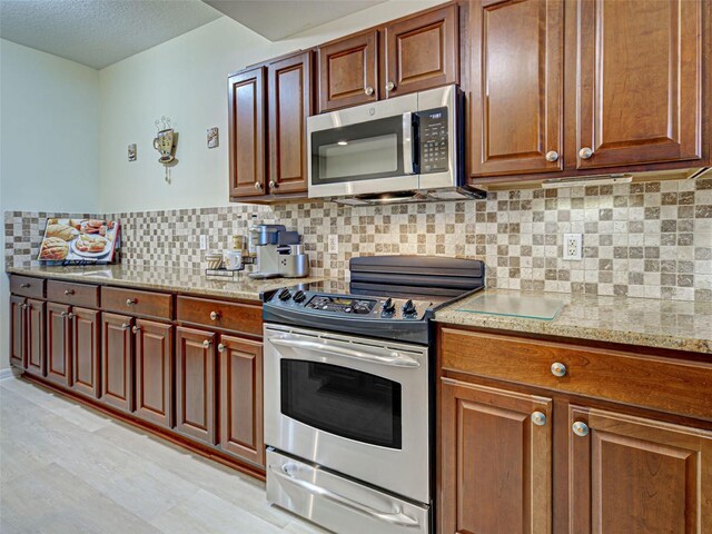 516 Tamiami Trl S Unit 303, Nokomis, FL 34275 - kitchen featuring stainless steel appliances, backsplash, light stone countertops, brown cabinetry, and a textured ceiling