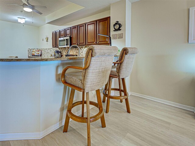 516 Tamiami Trl S Unit 303, Nokomis, FL 34275 - kitchen featuring stainless steel microwave, a breakfast bar, ceiling fan, decorative backsplash, and dark stone countertops