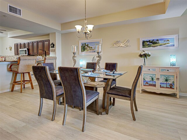 516 Tamiami Trl S Unit 303, Nokomis, FL 34275 - dining area with a chandelier, light wood-style floors, and a tray ceiling