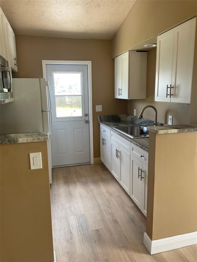 11248 Pendleton Ave Unit A & B, Englewood, FL 34224 - kitchen with a sink, light wood-style flooring, stainless steel microwave, white cabinets, and freestanding refrigerator