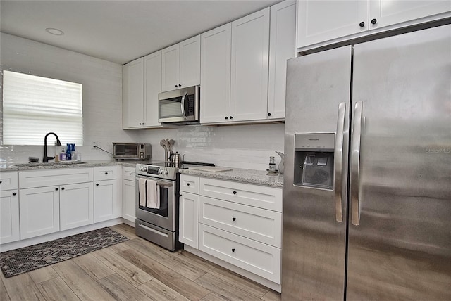 3340 Webber St, Sarasota, FL 34239 - kitchen featuring appliances with stainless steel finishes, a sink, white cabinets, light wood finished floors, and light stone countertops