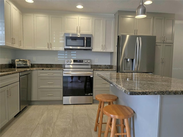 333 The Esplanade N Unit 102, Venice, FL 34285 - kitchen featuring appliances with stainless steel finishes, a breakfast bar, recessed lighting, dark stone counters, and hanging light fixtures
