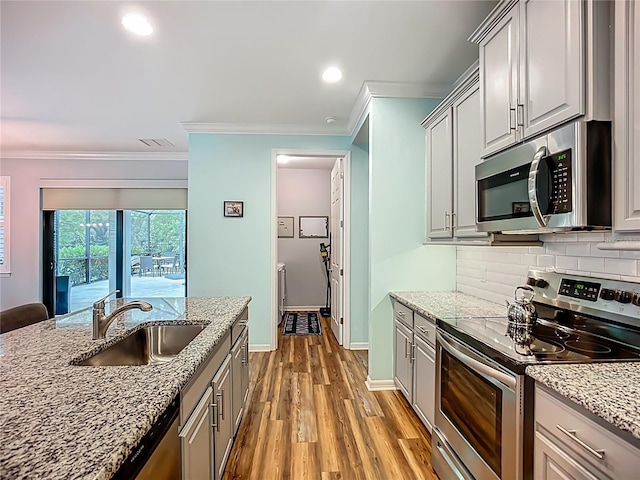 20749 Swallowtail Ct, Venice, FL 34293 - kitchen with appliances with stainless steel finishes, ornamental molding, wood finished floors, tasteful backsplash, and light stone counters