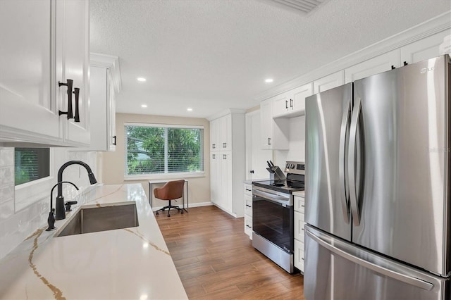 386 Nightingale Rd, Venice, FL 34293 - kitchen featuring stainless steel appliances, wood finished floors, white cabinets, light stone counters, and a textured ceiling