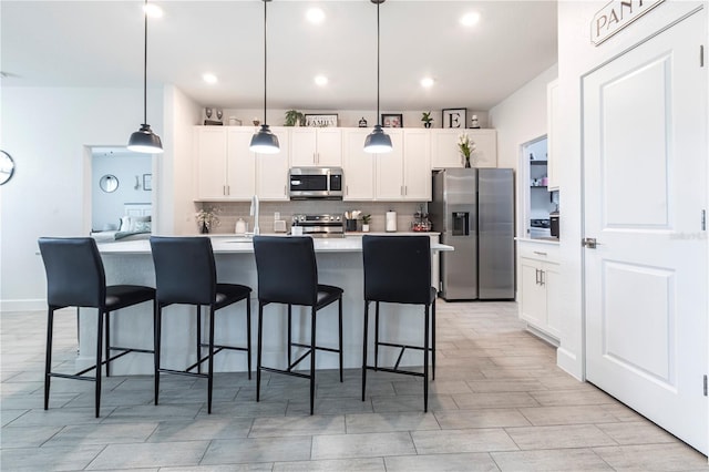 4033 Union Ln, North Port, FL 34288 - kitchen featuring stainless steel appliances, backsplash, a kitchen island with sink, white cabinets, and light countertops