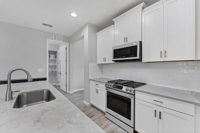 11240 Spring Gate Trl, Bradenton, FL 34211 - kitchen featuring stainless steel gas range, light stone counters, white cabinetry, light wood finished floors, and backsplash