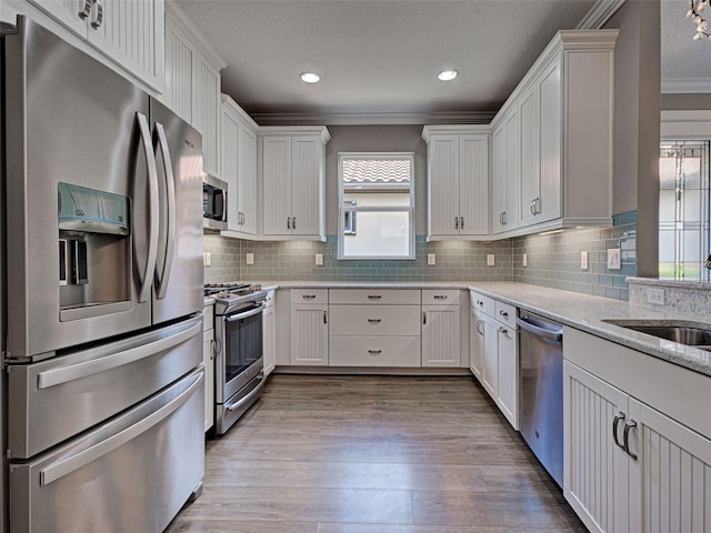 5832 Semolino St, Nokomis, FL 34275 - kitchen featuring stainless steel appliances, crown molding, white cabinetry, wood finished floors, and light stone counters