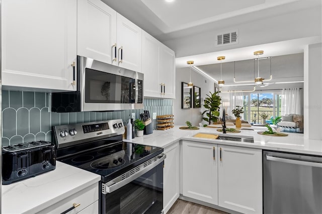 437 Cerromar Ln Unit 424, Venice, FL 34293 - kitchen featuring stainless steel appliances, white cabinets, a raised ceiling, backsplash, and decorative light fixtures