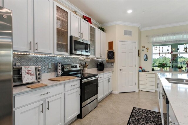 935 Tidewater Shrs Unit 721, Bradenton, FL 34208 - kitchen featuring stainless steel appliances, ornamental molding, tasteful backsplash, white cabinetry, and glass insert cabinets