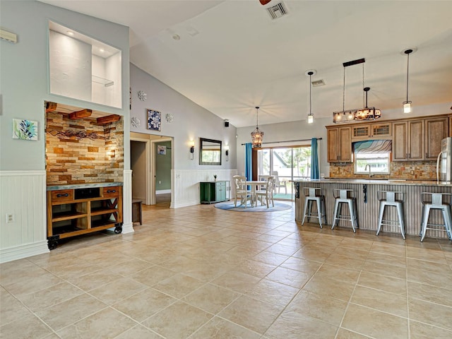 23102 Madelyn Ave, Port Charlotte, FL 33954 - kitchen featuring a kitchen bar, brown cabinets, a wainscoted wall, pendant lighting, and tasteful backsplash