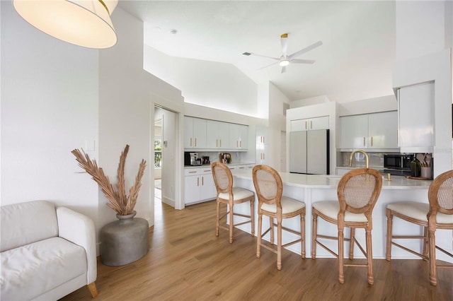 5028 Greenway Ct, North Port, FL 34287 - kitchen featuring freestanding refrigerator, black microwave, a peninsula, a breakfast bar, and high vaulted ceiling