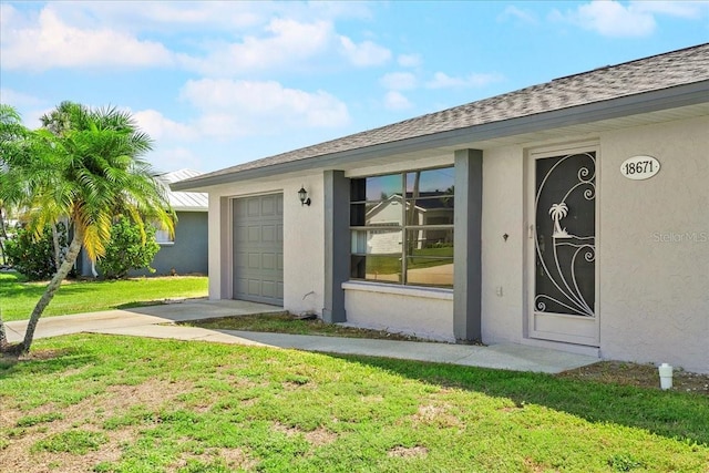18671 Macgill Ave, Port Charlotte, FL 33948 - doorway to property featuring stucco siding, a lawn, driveway, and an attached garage