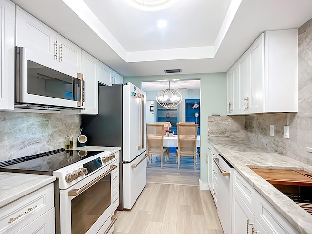 3274 Savage Rd, Sarasota, FL 34231 - kitchen with white appliances, a tray ceiling, white cabinetry, light stone counters, and a chandelier