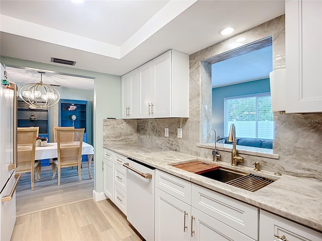 3274 Savage Rd, Sarasota, FL 34231 - kitchen featuring white dishwasher, white cabinetry, a chandelier, light wood-style floors, and decorative backsplash