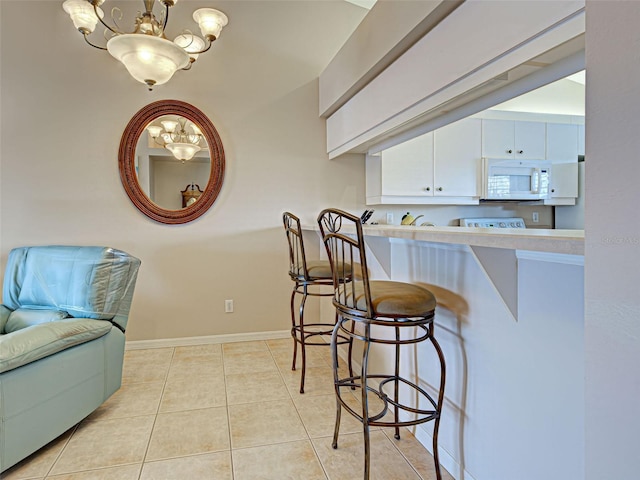 903 Addington Ct Unit 203, Venice, FL 34293 - kitchen with white microwave, a chandelier, a kitchen bar, white cabinetry, and light tile patterned floors