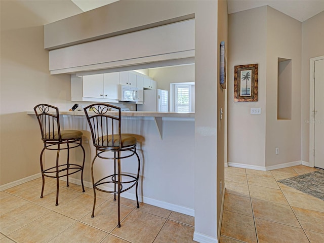 903 Addington Ct Unit 203, Venice, FL 34293 - kitchen with white appliances, light tile patterned floors, a kitchen bar, and white cabinets
