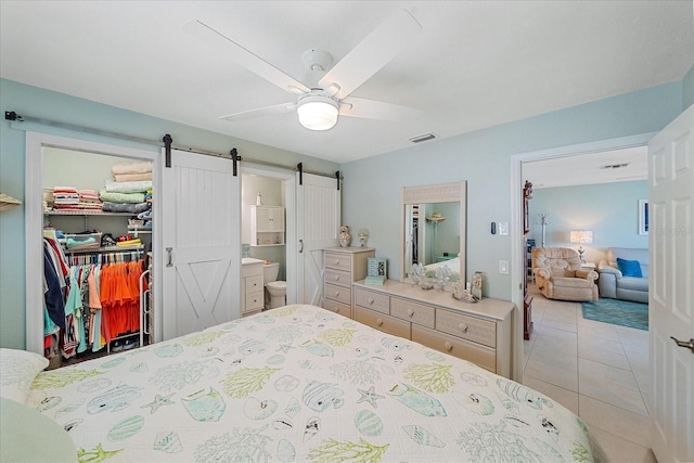 10341 Greenway Ave, Englewood, FL 34224 - bedroom featuring a barn door, a spacious closet, tile patterned flooring, ensuite bath, and ceiling fan