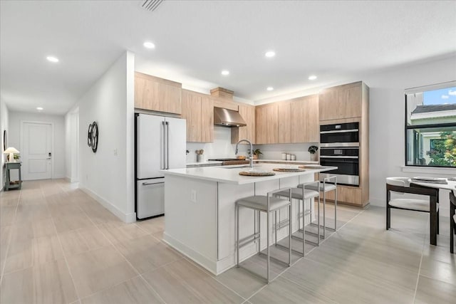18525 Midsummer Pl, Venice, FL 34293 - kitchen with high end white refrigerator, exhaust hood, light brown cabinetry, light countertops, and a kitchen bar
