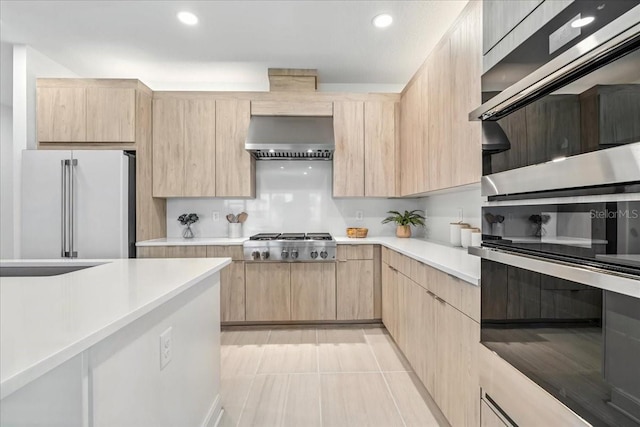 18525 Midsummer Pl, Venice, FL 34293 - kitchen with light brown cabinetry, appliances with stainless steel finishes, wall chimney exhaust hood, light countertops, and recessed lighting