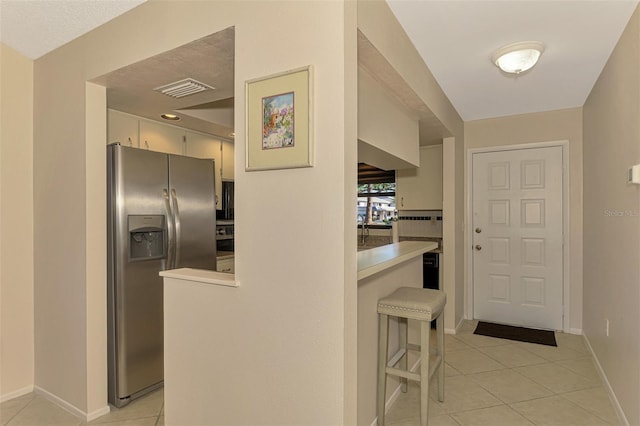 927 Capri Isles Blvd Unit 5, Venice, FL 34292 - kitchen with stainless steel fridge with ice dispenser, light tile patterned floors, light countertops, and a kitchen breakfast bar