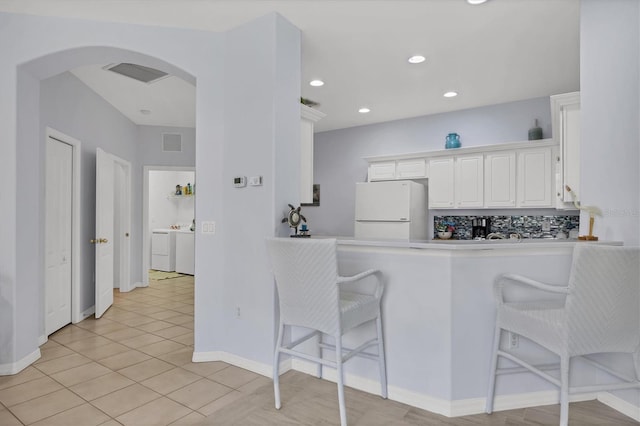 4841 Whispering Oaks Dr, North Port, FL 34287 - kitchen featuring freestanding refrigerator, a breakfast bar, arched walkways, independent washer and dryer, and white cabinets