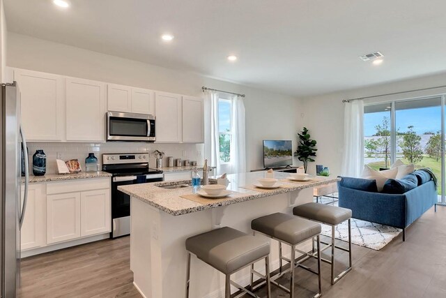 kitchen with light hardwood / wood-style floors, white cabinets, appliances with stainless steel finishes, and a center island with sink