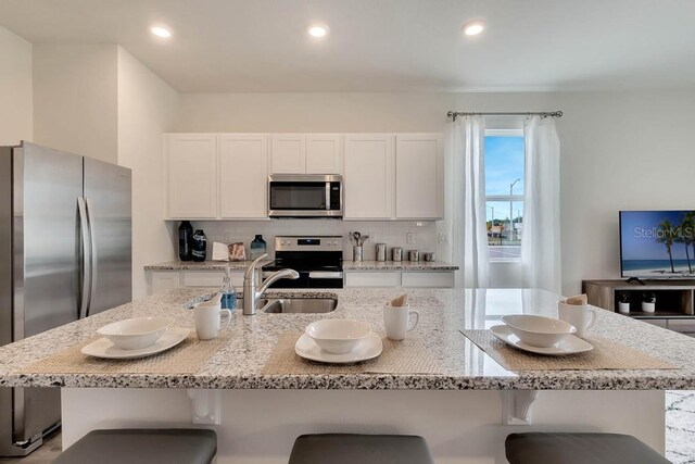 kitchen featuring a kitchen bar, tasteful backsplash, appliances with stainless steel finishes, and white cabinetry