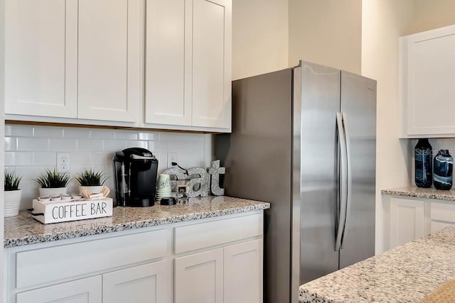 kitchen featuring stainless steel fridge, backsplash, and white cabinets