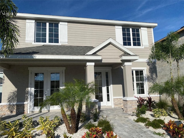 view of front facade with stone siding, french doors, a shingled roof, and stucco siding