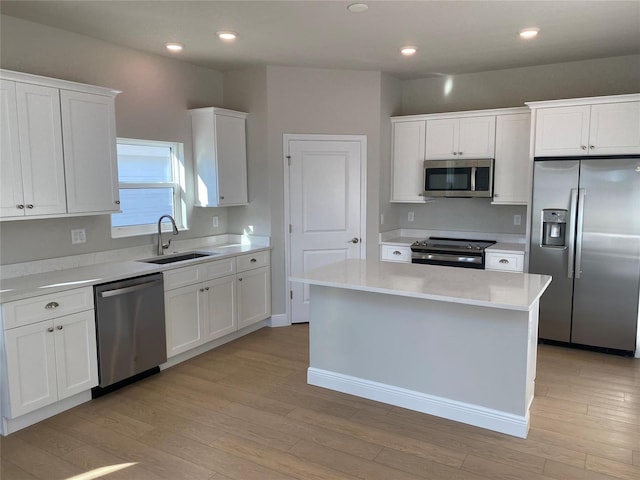 kitchen with stainless steel appliances, light countertops, white cabinetry, a kitchen island, and a sink