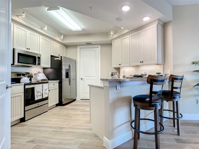 kitchen with white cabinetry, a breakfast bar, appliances with stainless steel finishes, and light stone counters