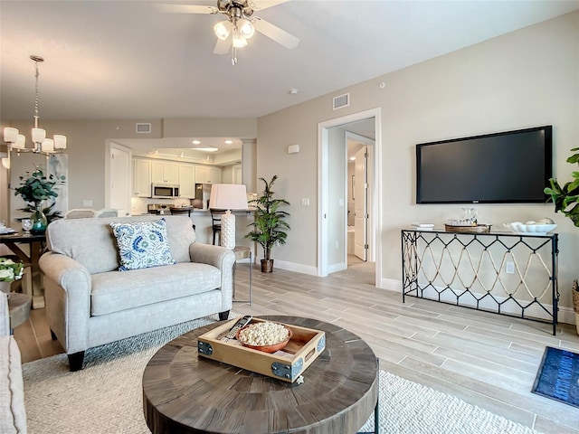 living room featuring decorative columns, light wood-type flooring, and ceiling fan with notable chandelier