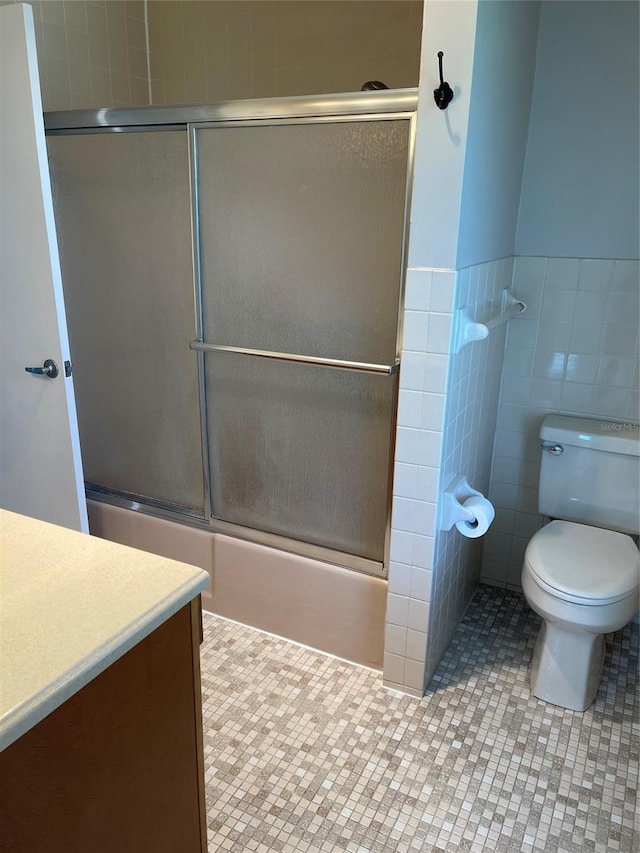 full bathroom featuring toilet, shower / bath combination with glass door, vanity, tile walls, and tile flooring