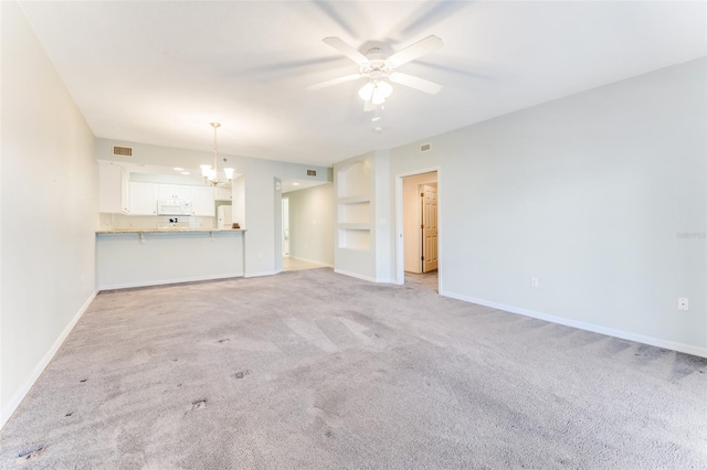 unfurnished living room featuring light carpet, ceiling fan with notable chandelier, and built in shelves