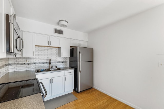 kitchen with white cabinetry, backsplash, appliances with stainless steel finishes, light hardwood / wood-style floors, and sink