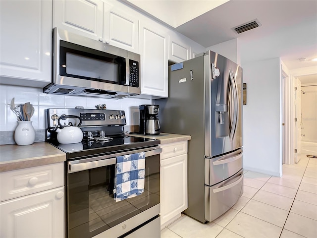 kitchen featuring white cabinets, decorative backsplash, light tile patterned flooring, and appliances with stainless steel finishes