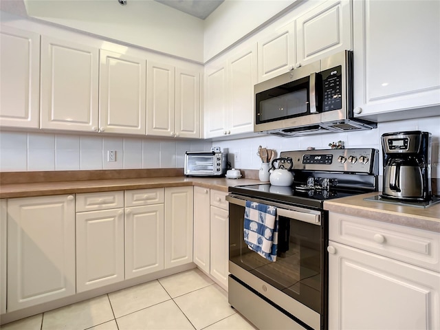 kitchen featuring decorative backsplash, appliances with stainless steel finishes, white cabinetry, and light tile patterned flooring