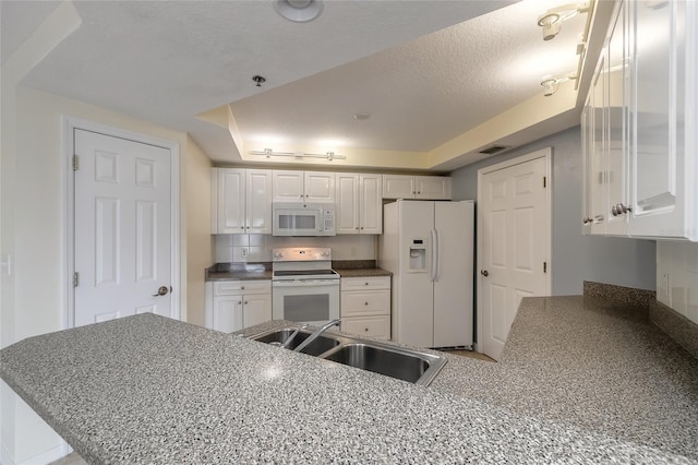 kitchen featuring white cabinetry, a tray ceiling, white appliances, sink, and kitchen peninsula