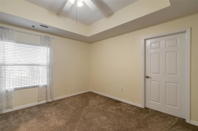 spare room featuring a tray ceiling, dark carpet, and ceiling fan