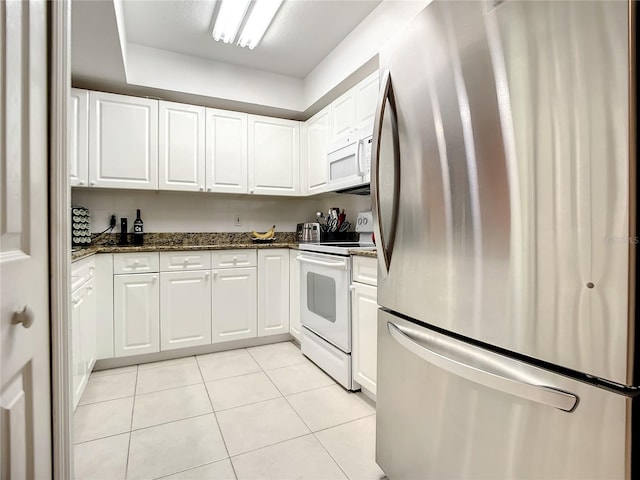 kitchen with white appliances, dark stone counters, light tile patterned floors, and white cabinets