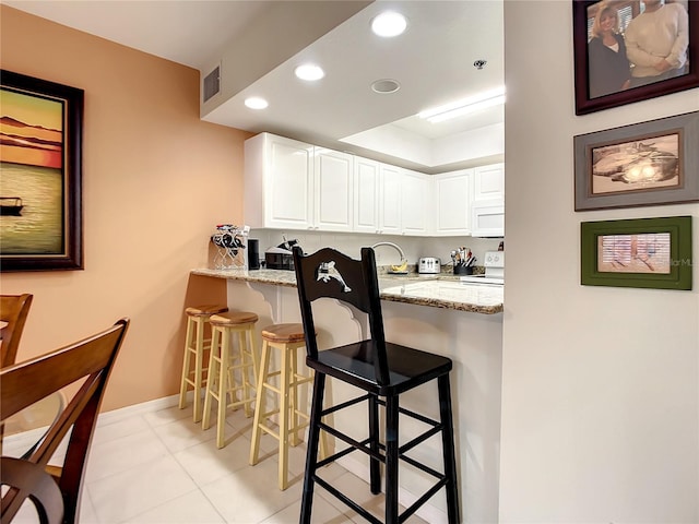 kitchen featuring white appliances, a kitchen bar, light stone countertops, and white cabinets